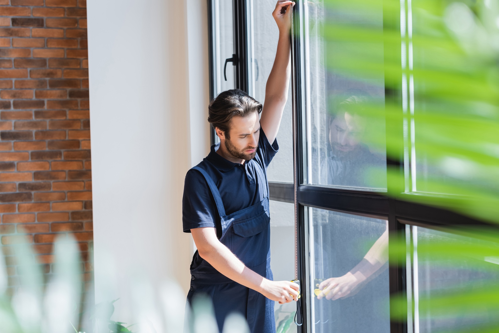 workman measuring large windows on blurred foreground